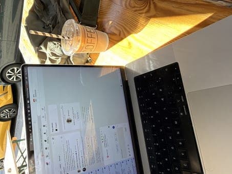 MacBook, iced coffee, and bag on a wooden table